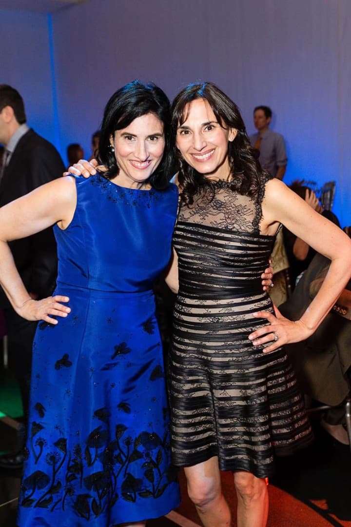 Two women posing together at a party, one in blue and one in black lace