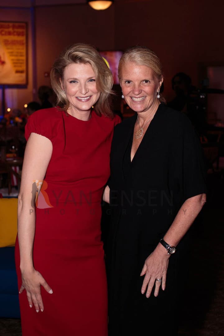 Two women smiling together at a party, one in red and one in black