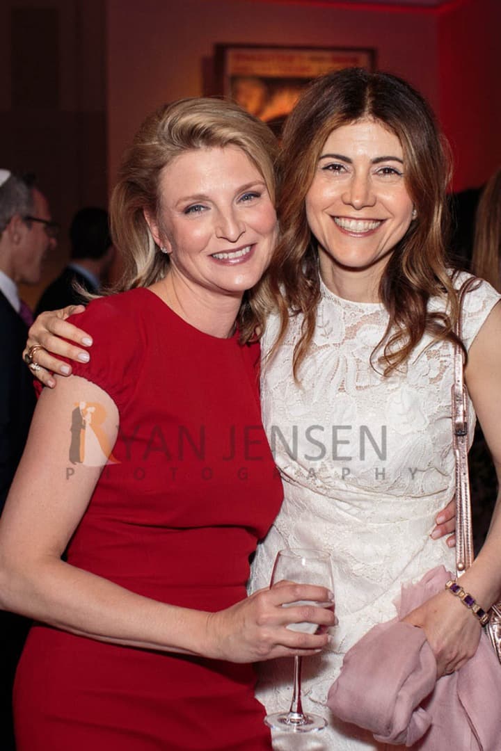Two women hugging at a party, one in red and one in white lace