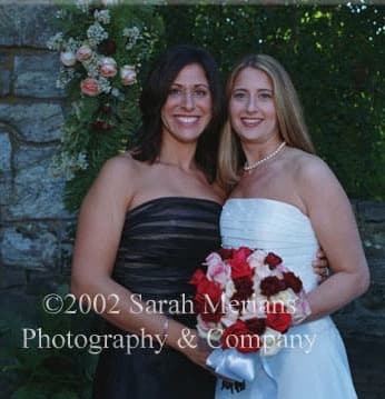 Bride with a woman in a dark strapless dress, holding red and pink roses